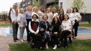 Group of fourteen adults wearing traditional embroidered clothing, posing outdoors by a pool in a residential courtyard.