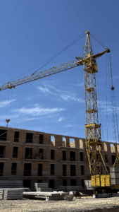 Yellow tower crane over an unfinished brick building under a clear blue sky, with stacked concrete blocks on the ground.