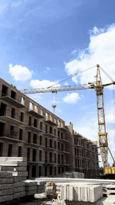 Under-construction brick building with multiple floors and a crane lifting materials against a blue sky.
