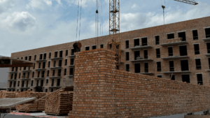 Construction site with a brick building under construction, crane overhead, and piles of bricks in the foreground.