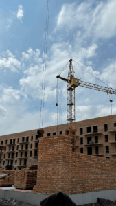 Construction site with a tall crane assembling a brick building under a blue sky with scattered clouds.